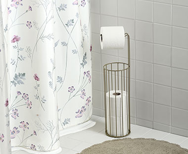 Weißer Duschvorhang mit Blumenmuster hinter einem Toilettenpapiershalter aus Messing 