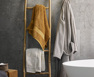 Handtücher aus 100% Baumwolle in Grau und Gelb an einer Wand hängend