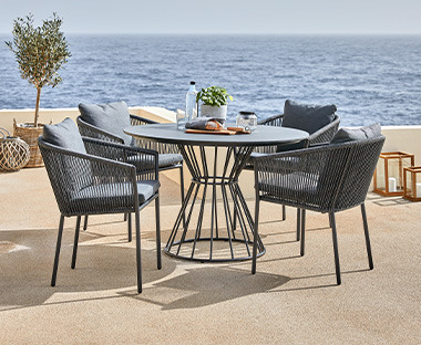 Runder Gartentisch und vier Gartenstühle auf einer Terrasse mit Blick aufs Meer