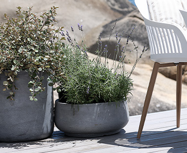 Zwei Pflanzkübel in Beton-Optik neben einem Gartenstuhl