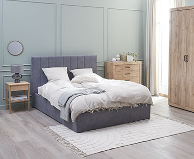 Bett mit grauem Stoffbezug und Schlafzimmermöbel aus Holz