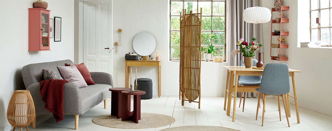 Wohn-/Esszimmer mit rosafarbenem Hängeschrank, grauem Schlafsofa, Bambus-Paravent, Bambus-Schreibtisch und grauen Esszimmerstühlen