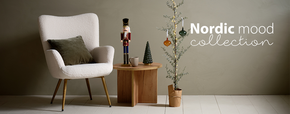 Sessel mit Kissen, Couchtisch mit Weihnachtsfigur und ein kleiner, mit Glaskugeln geschmückter Weihnachtsbaum