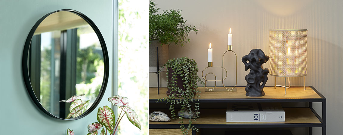 Runder Spiegel an grüner Wand, kleine Tischlampe und Kerzenhalter 