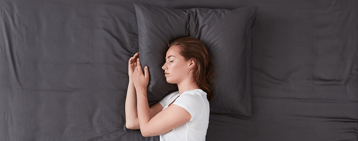 Schlafende Frau im Bett mit dunkelgrauer Bettwäsche
