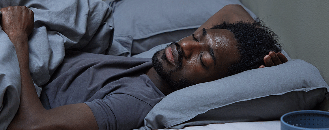 Mann schläft in einem Bett mit einer grauen Bettwäsche