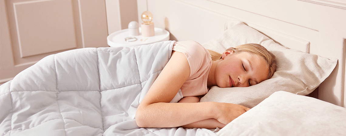 Eine Frau schläft auf der Seite im Bett mit einer Gewichtsdecke