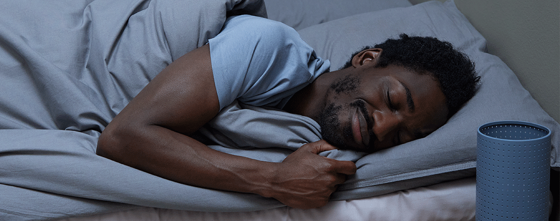 Mann schläft in Seitenlage in Bett mit grauer Bettdecke und Kopfkissen