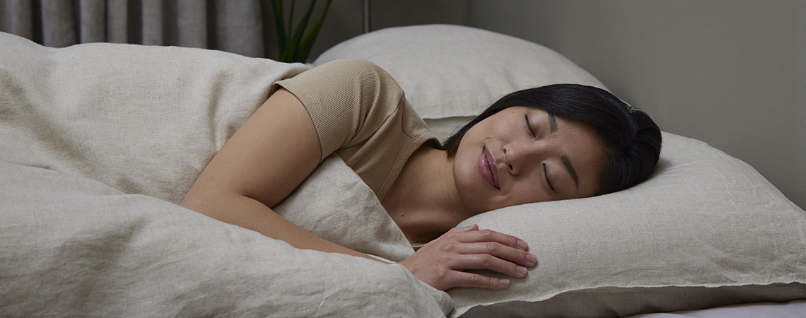 Frau schläft friedlich auf der Seite in Bettwäsche aus Leinen