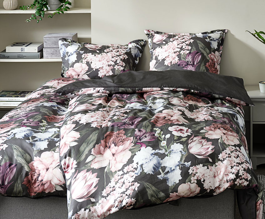 Bettwäsche mit Blumenmuster auf einem grauem Bett