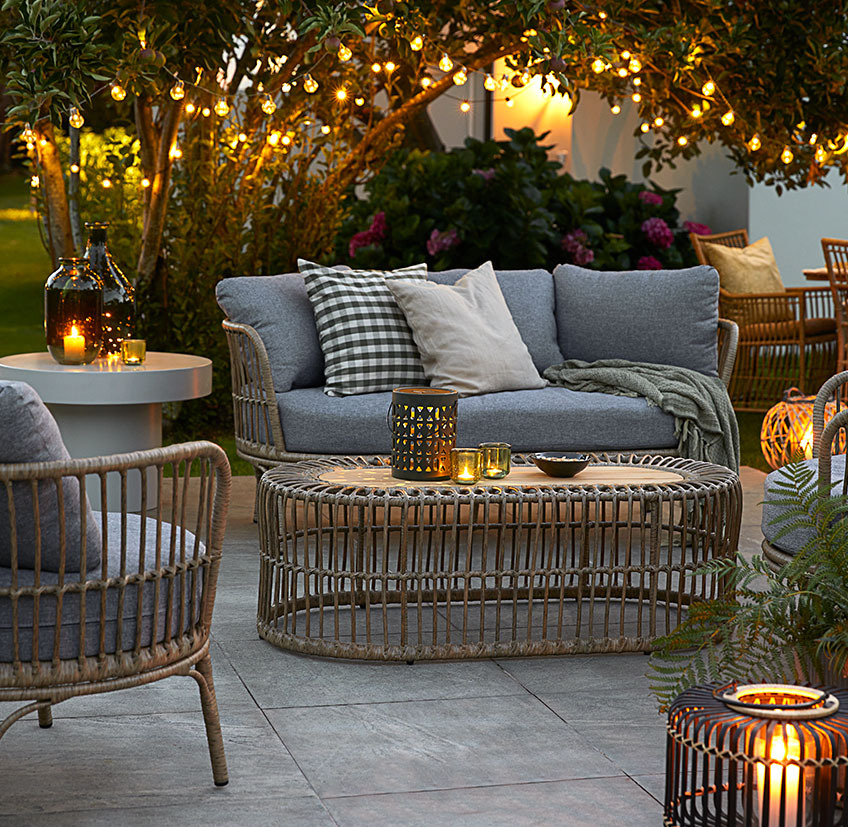 Gemütliche Loungemöbel auf der Terrasse mit Lichterketten, Batterielampen und Windlichtern mit Kerzen und Teelichtern