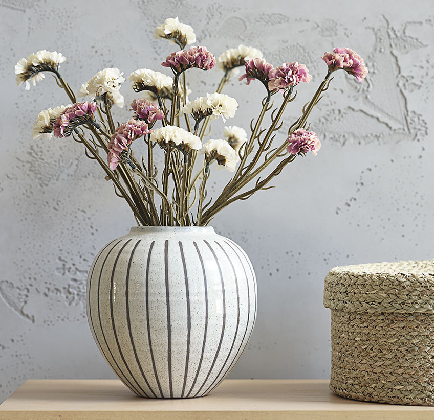 Rosa und weiße Kunstblumen in weißer Vase mit grauem Streifenmuster