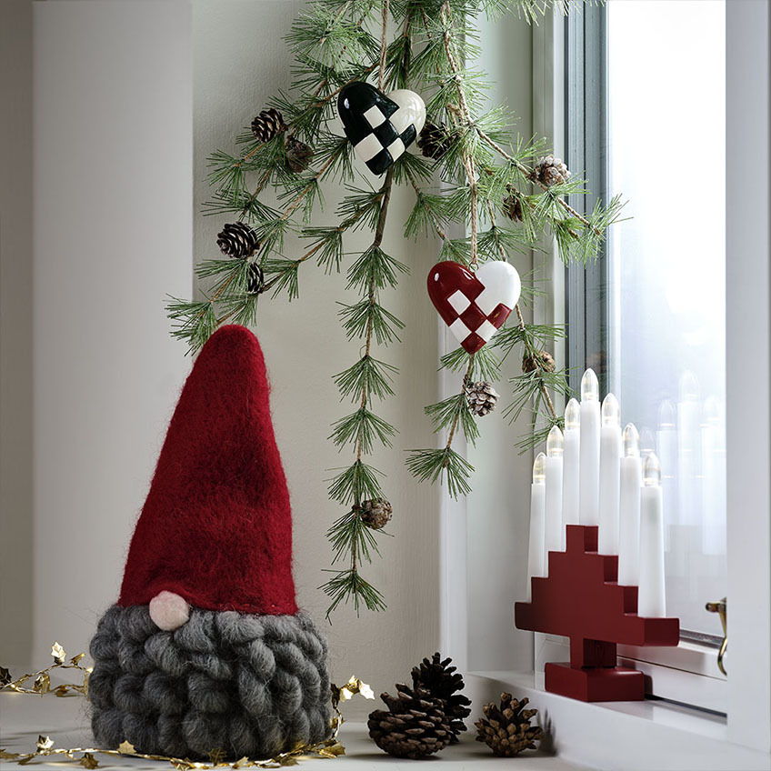 Weihnachtswichtel mit roter Mütze und grauem Bart, Weihnachtsherz-Deko und roter Lichterbogen
