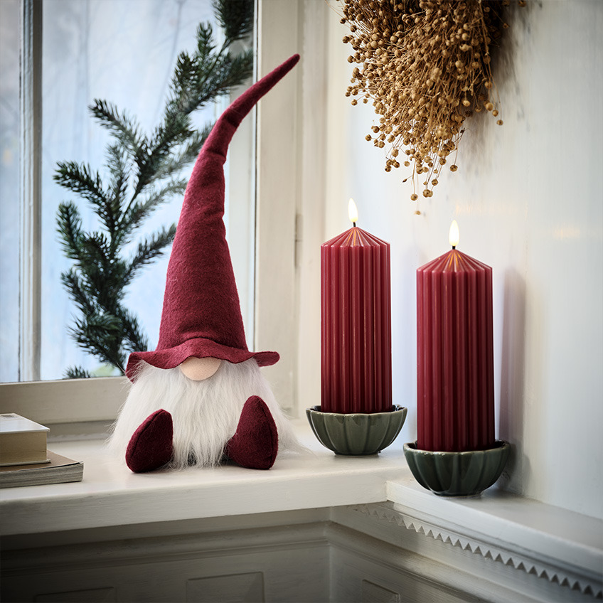 Skandinavischer Weihnachtswichtel auf der Fensterbank neben großen, roten Kerzen