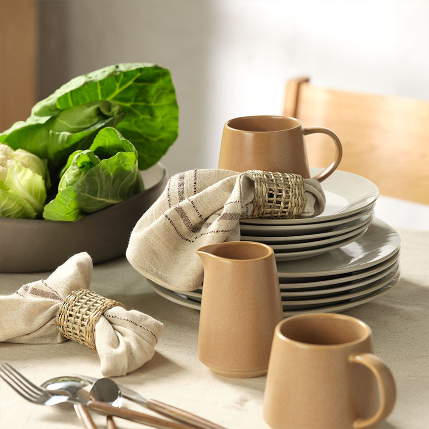 Becher, Milchkännchen, Stoffservietten mit Serviettenringen und Salatschüssel auf dem Esstisch