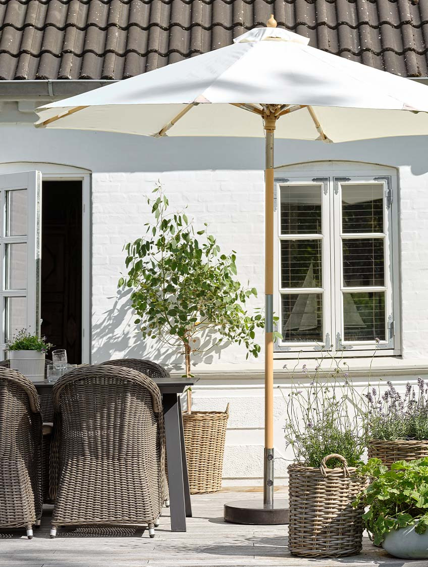 Klassischer cremefarbener Sonnenschirm auf der Terrasse mit Gartentisch und Gartenstühlen