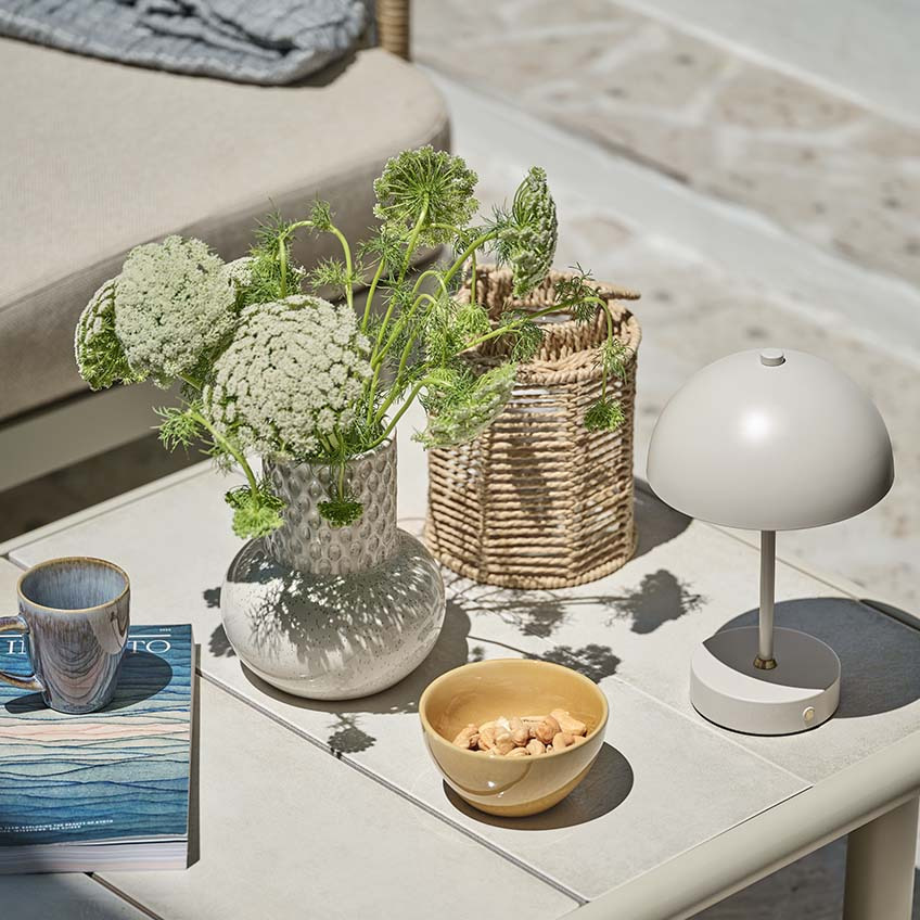 Kleiner Gartentisch mit verschiedenen Dekorationen, darunter eine kleine Batterielampe, eine Vase und eine Laterne