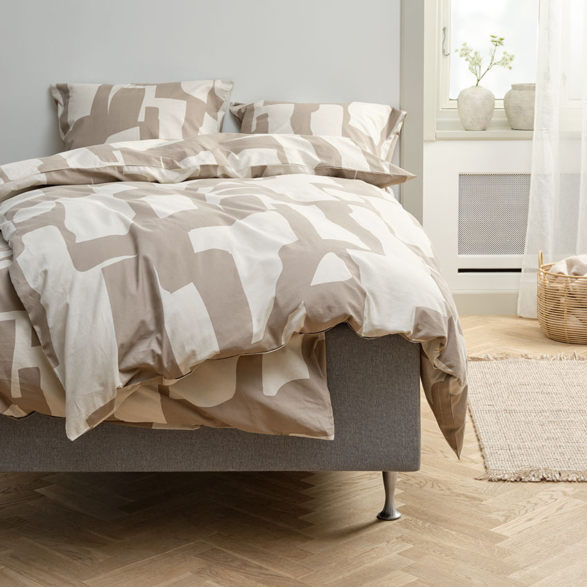 Bettwäsche in dunklem Sand und Beige mit grafischem Muster auf dem Bett im Schlafzimmer