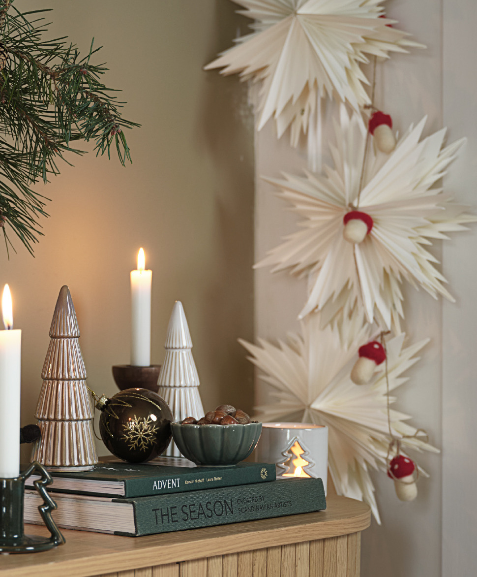 SKRYMSLI Papiersterne und LODUR Girlande mit Fliegenpilzen Ein Sideboard mit schönem Weihnachtsschmuck und Papiersternen an der Wand