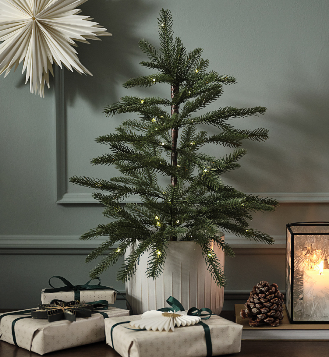 Künstlicher Weihnachtsbaum in einem Topf und einem Papierstern an der Wand 