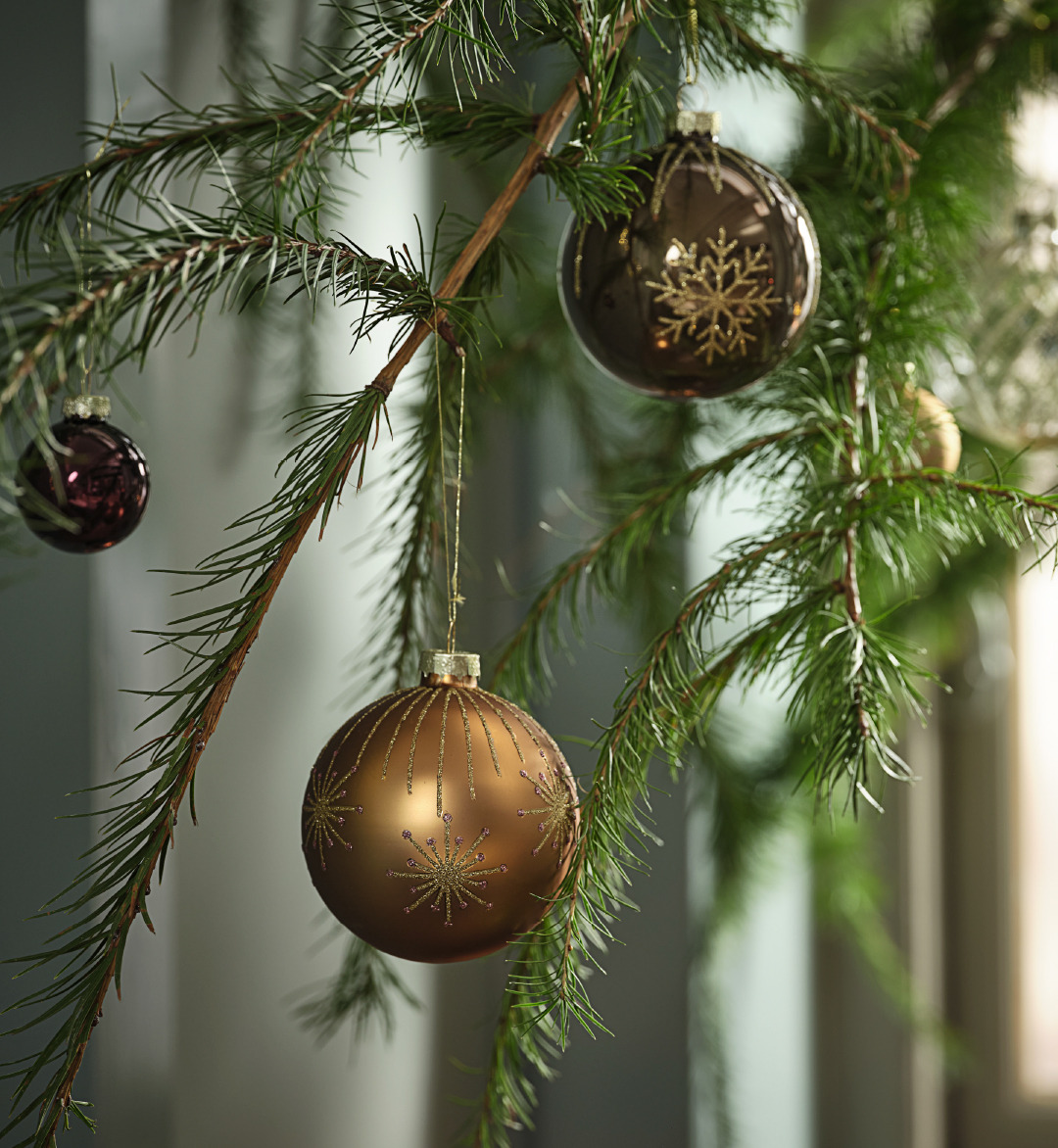 Ein mit Christbaumkugeln in Erdtönen und Glitzer geschmückter Zweig