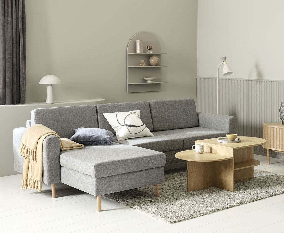 Graues Chaiselongue-Sofa in einem Wohnzimmer mit Couchtisch, Lampen und Wohnaccessoires