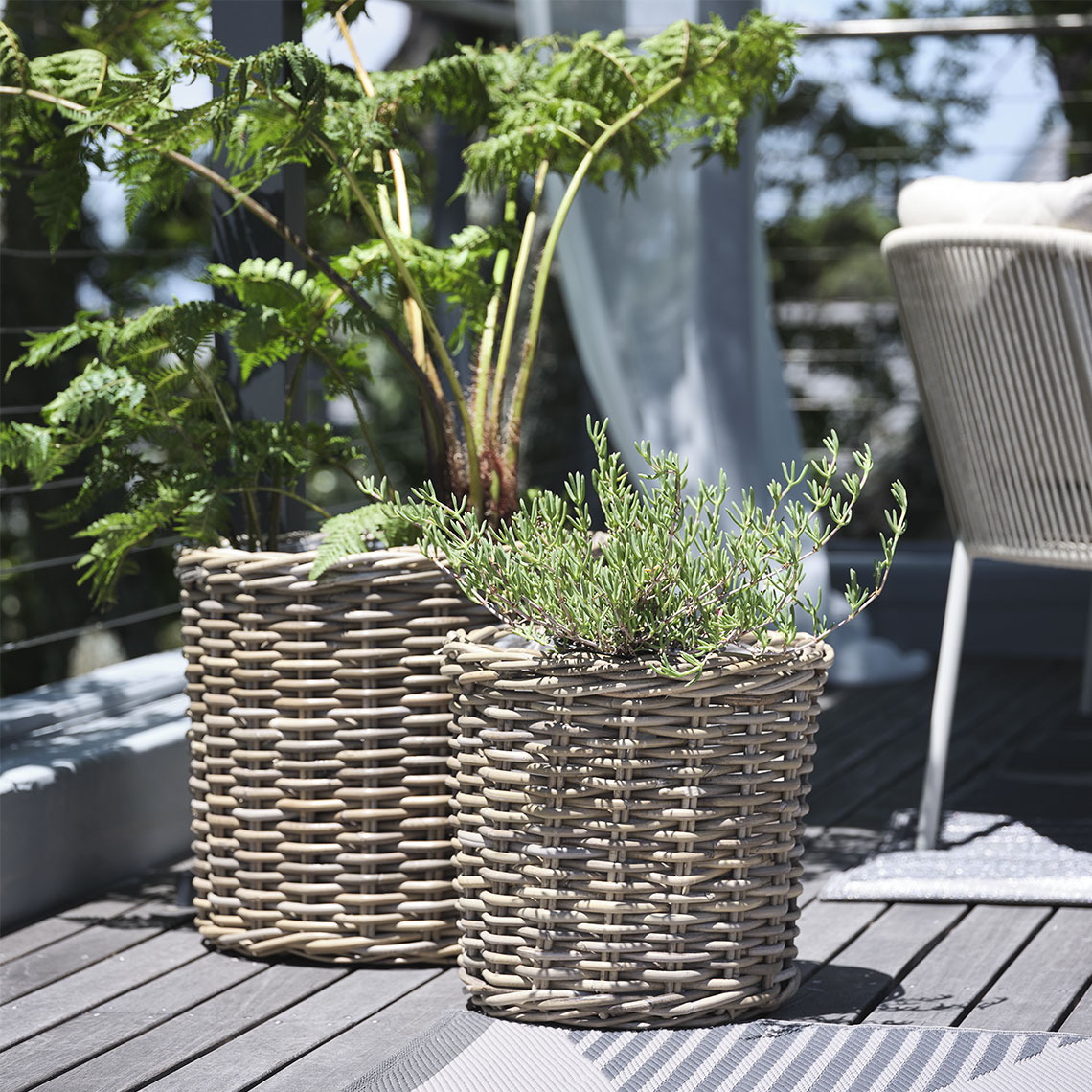Pflanzkörbe SEGLA Zwei Pflanzkörbe aus natürlichem, unbehandeltem Rattan stehen auf einem Balkon mit Pflanzen