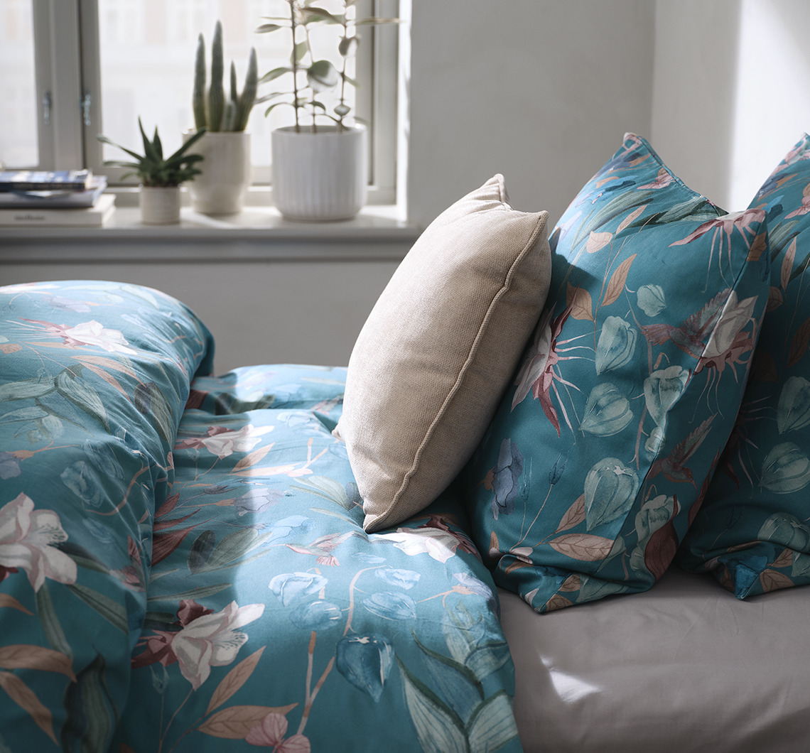 Kombiniere BERTHA mit monochromen Artikeln für einen dynamischen Look Schlafzimmer mit geblümter Bettwäsche und zusätzlichem Kissen in einer Kontrastfarbe