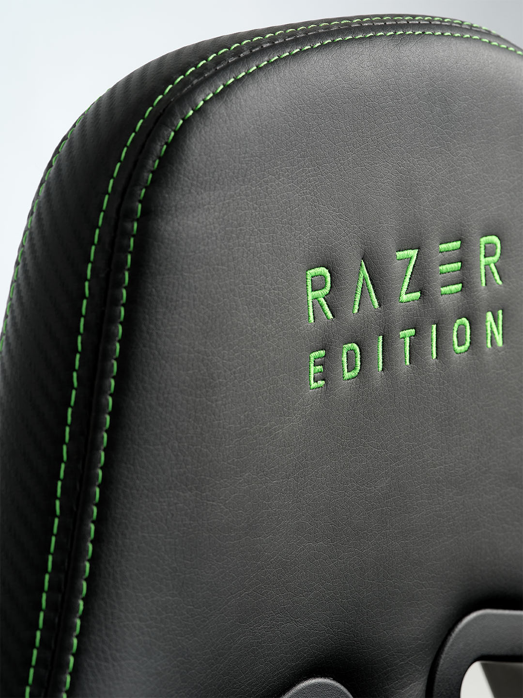 Nahaufnahme eines schwarzen Razer-Gaming-Stuhls mit grünen Nähten und der Aufschrift „RAZER EDITION” in grüner Stickerei auf der Rückenlehne.
