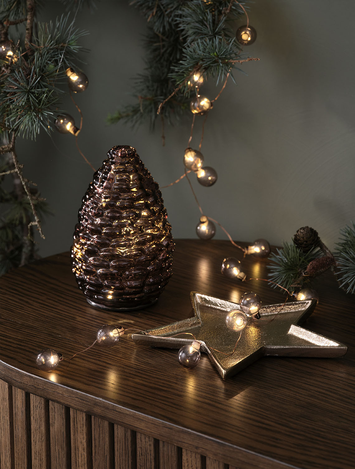 LED-Tannenzapfen DELLING und Lichterkette ALV  Dekorative Weihnachtsbeleuchtung wie ein Deko-Tannenzapfen- und goldene Lichterkette mit Weihnachtskugeln auf einer Anrichte