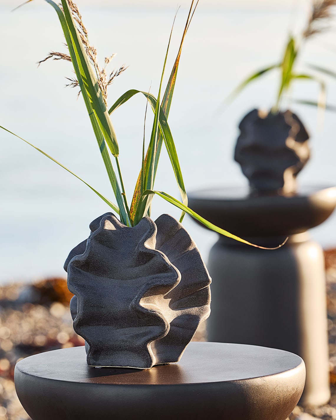  Organisch geformte Vase auf Sockel an einem Strand