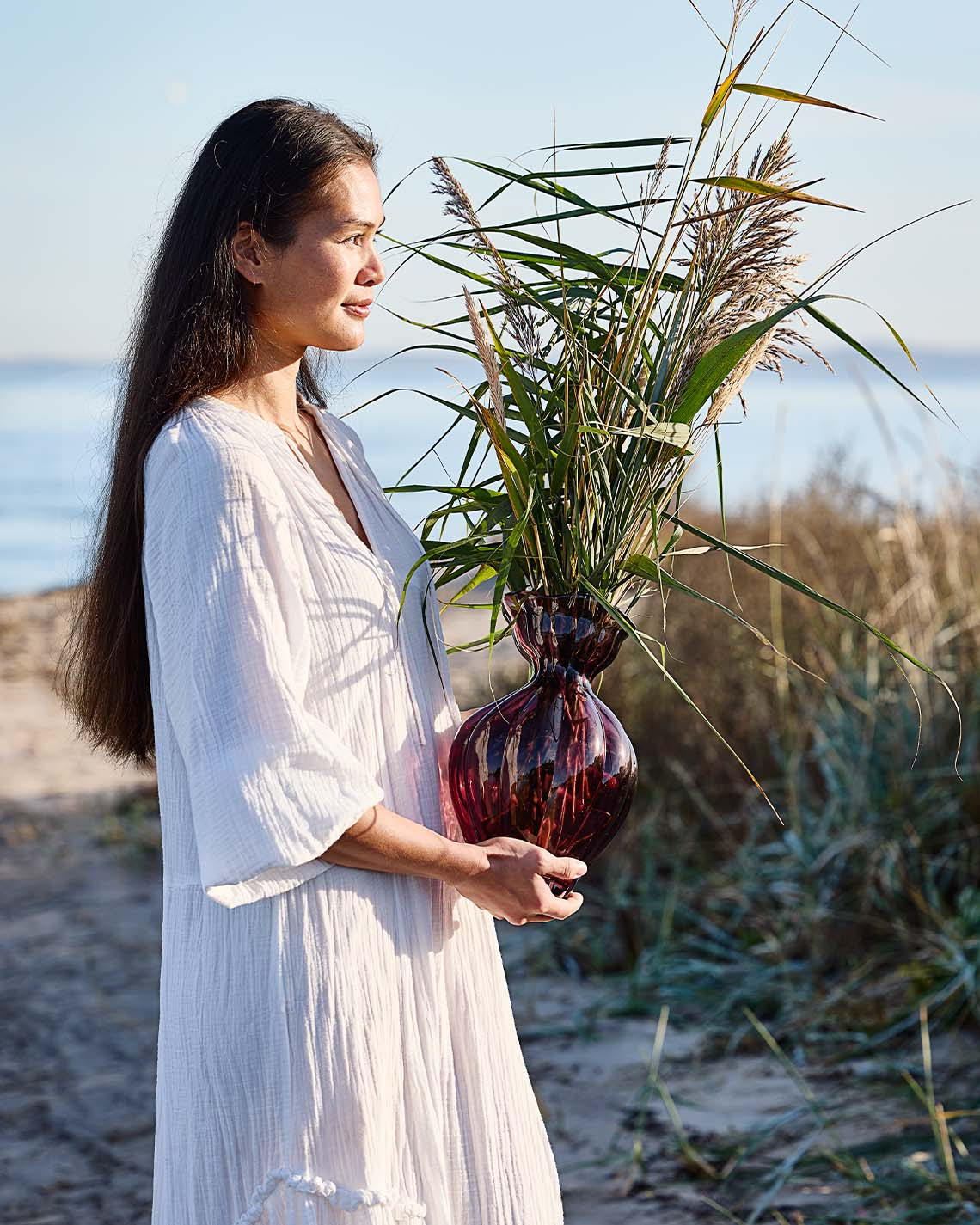 Frau hält Glasvase mit organischer Form am Strand    
