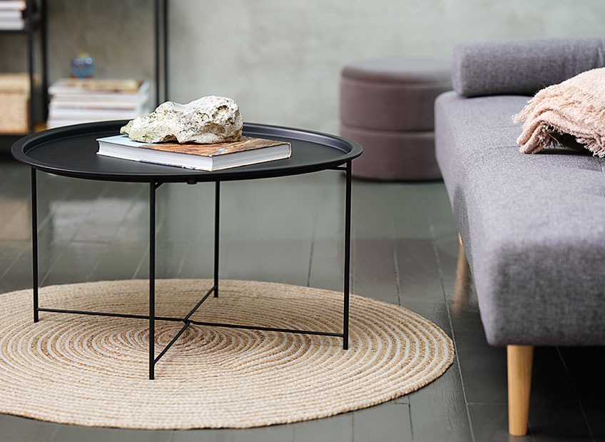 Ein Couchtisch auf einem runden Teppich vor einem Sofa 