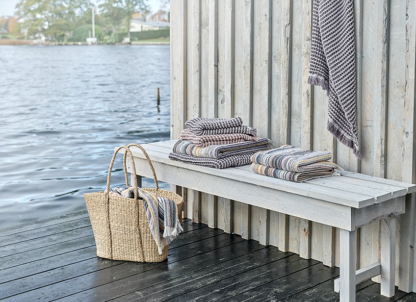 Luxuriöse Handtücher auf einer Bank und in einer Korbtasche an einem See