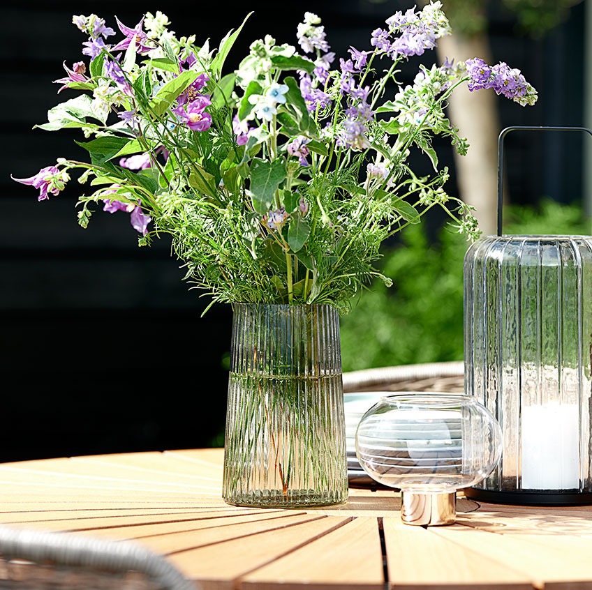 Glasvase und Windlichter auf einem runden Gartentisch 