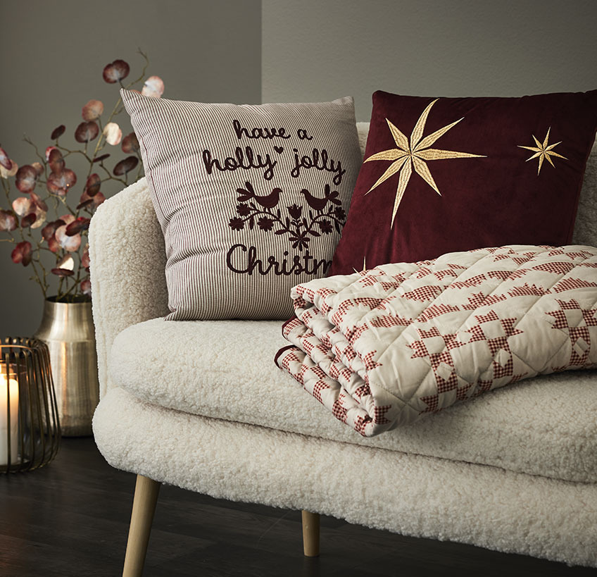Kissen und Steppdecke mit Weihnachtsmotiven auf einem weißen Sofa