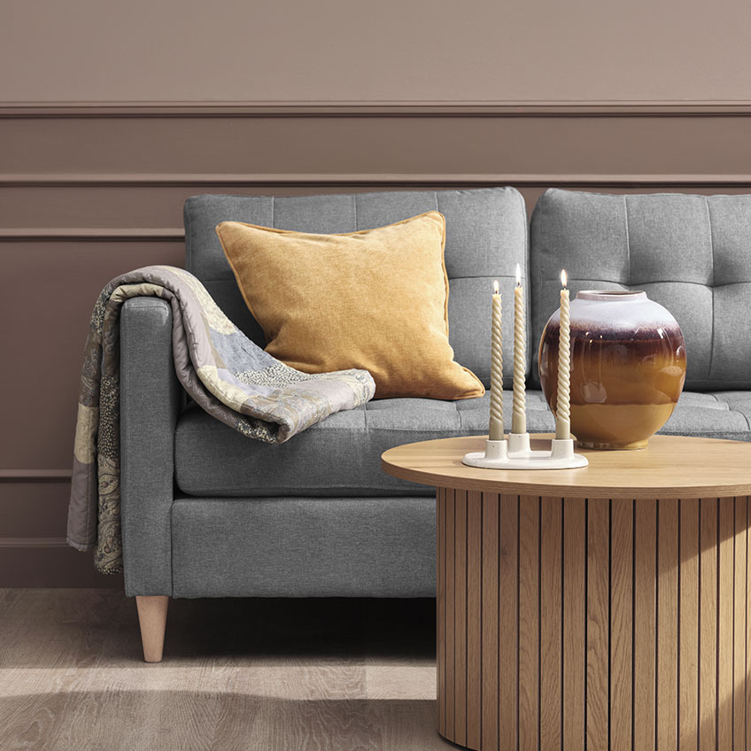 Steppdecke HUMLE und Zierkissen HORNFIOL Steppdecke und gelbes Zierkissen auf einem grauen Sofa, Couchtisch aus Holz mit Vase und Kerzen darauf