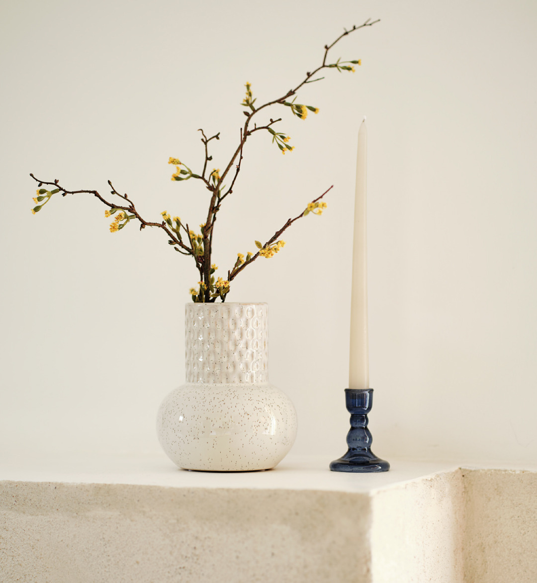 Vase mit Zeig neben einem Kerzenständer auf einer Mauer