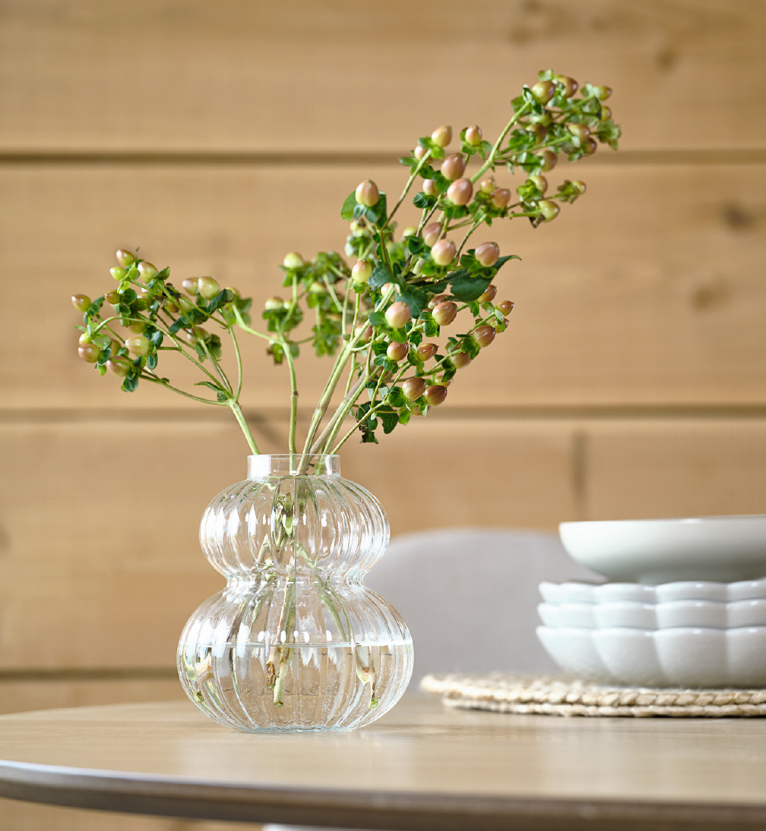 Kleine Glasvase mit grüner Blume auf einem Tisch