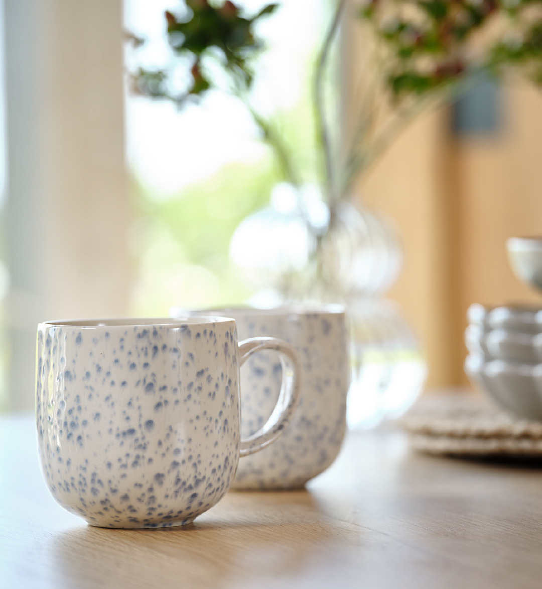 Zwei Becher in Weiß mit blauen Akzenten auf einem Esstisch