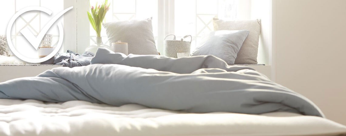 Gemütliches Bett mit weißer und blauer Bettwäsche im Morgenlicht