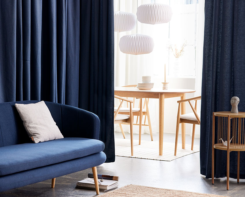 Blauer Vorhang hinter einem Sofa trennt einen Wohnbereich von einem Essbereich