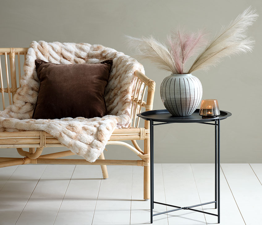 Sofa mit Kuscheldecke aus Kunstfell und braunem Kissen. Schwarzer Beistelltisch mit Vase und Teelichthalter