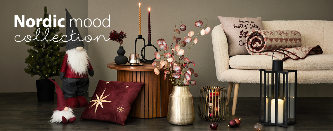 Weihnachtswichtel, Kissen, goldene Vase mit Kunstblume, goldener Kerzenständer und schwarze Laterne vor einem weißen Sofa