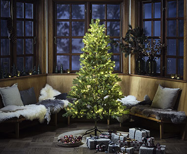 Beleuchteter Weihnachtsbaum NIDUD in der Mitte eines Raumes vor einer Bank stehend