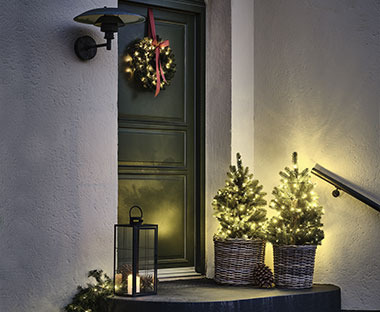 Stimmungsvoll beleuchteter Eingangsbereich mit Lichterketten, Weihnachtskranz und künstlichem Baum