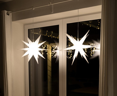 Leuchtende Weihnachtssterne an einer Vorhangstange vor einem Fenster hängend