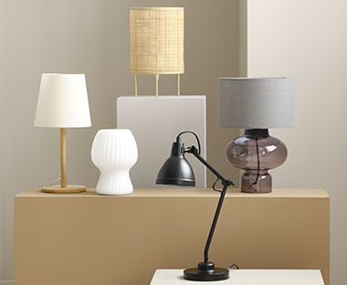 Tischlampen in verschiedenen Designs auf und vor einem Podest