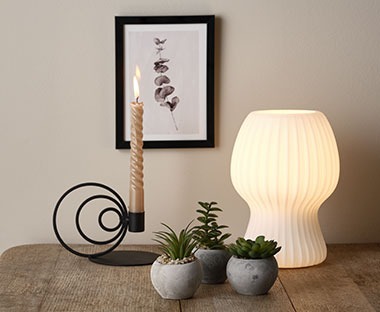 Tischlampe aus Glas mit Kunstpflanzen und einem modernen Kerzenständer auf einem Tisch