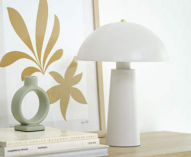 Tischlampe in Weiß auf einer Anrichtevor einem Bilderrahmen und neben einen Kerzenständer